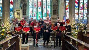 Saxophonics band, standing playing a selection of saxophones, whearing santa hats and tinsel in front of the church altar